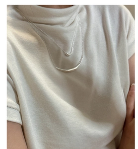 Detail of layered S925 silver smile necklaces on a white t-shirt for a minimalist look