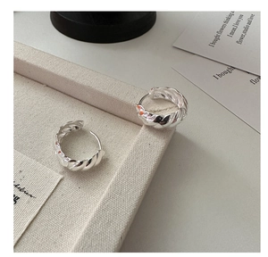 Macro view of chunky silver twisted croissant hoop earrings on a beige fabric tray