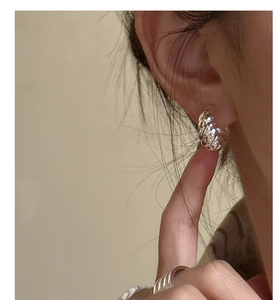 Macro shot of silver croissant earrings and textured ring worn on model with soft lighting