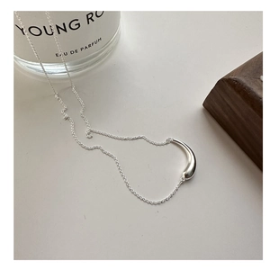 Detail view of a polished silver smile pendant necklace on a minimalist wooden prop