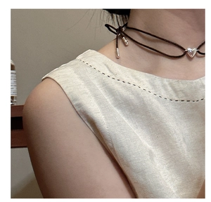 Detail eines silbernen Herzanhängers an einem dunkelbraunen Choker am Hals