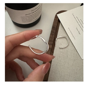Macro detail of irregular wave-shaped silver hoop earrings on minimalist decor
