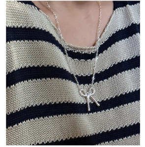 Detail of silver twisted bow necklace pendant worn on neck with stylish texture