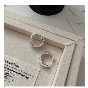 Macro shot of silver twisted rope hoop earrings on a beige canvas jewelry display tray