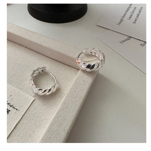 Macro detail of S925 sterling silver twisted hoop earrings on a beige linen tray