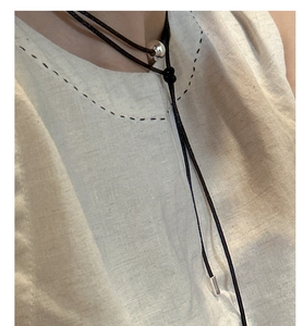 Detail of minimalist black cord necklace featuring a polished silver ball pendant on model