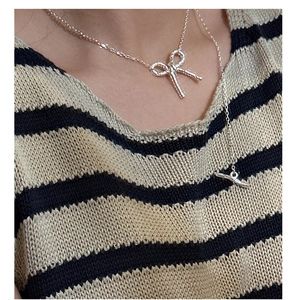 Detail of silver S925 bow necklace with molten texture on a model wearing striped sweater