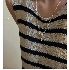 Close-up of a silver bow knot pendant necklace worn over a striped knit sweater