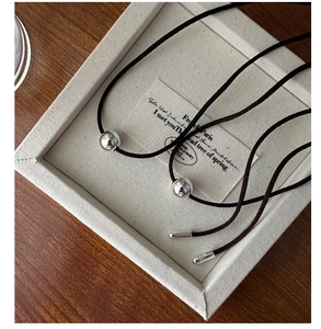 Close-up of a high-polish silver bead pendant on a black cord with metal end caps
