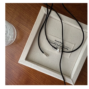 Detail of adjustable black cord necklace with silver beads on a minimalist wood surface
