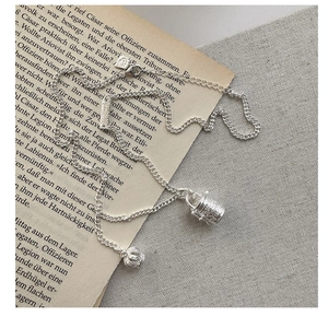 Close-up of S925 silver necklace with bucket bead and crown pendant on vintage paper