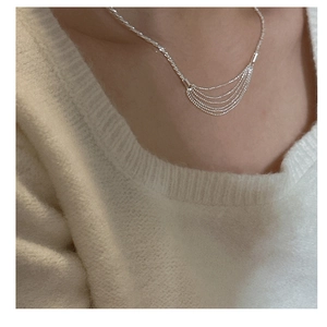 Detail of layered S925 sterling silver tassel necklace worn on model's neckline