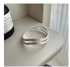Macro shot of silver S925 textured wave-layered bangle next to a black perfume bottle