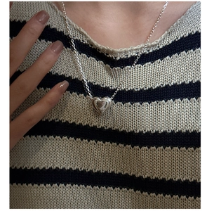 Détail d'un collier pendentif cœur en argent S925 porté sur un pull en maille rayé