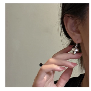 Close-up of a silver mushroom hook earring and a black bead ring worn by a model