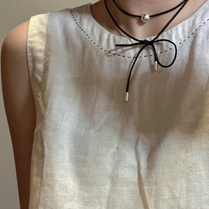 Choker necklace featuring a black cord and a silver bead on a woman in linen clothing