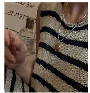 Dettaglio ravvicinato di una collana a cuore bicolore argento e oro su abito a righe