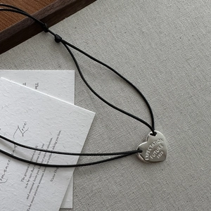 Macro detail of S925 silver heart pendant with engraved text on a textured linen background