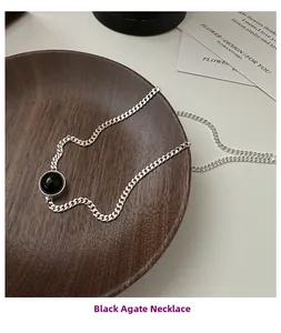 Detailed view of a black agate pendant on a silver chunky link chain over wood