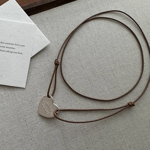 Detail of silver heart pendant with Expectation Future engraving on brown leather cord