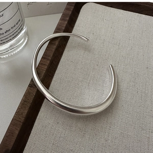 Detail of minimalist matte S925 silver open bangle on a rustic wooden jewelry tray