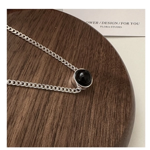 Close-up of S925 sterling silver chain with round black agate pendant on a wooden display