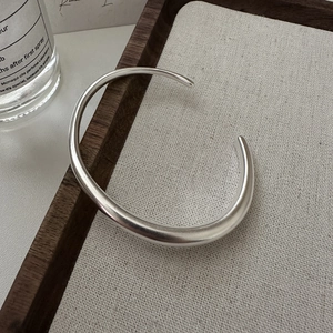 Minimalist S925 sterling silver open bangle with a matte finish on a wooden display