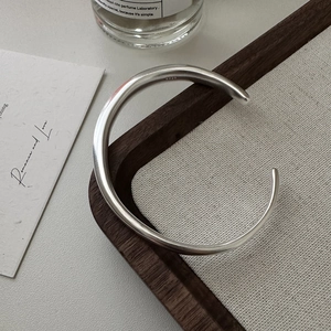 Minimalist S925 sterling silver open bangle with a smooth matte finish on a linen tray