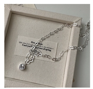 Gros plan du collier coeur en argent S925 avec pendentif en zircon sur présentoir beige