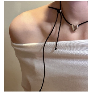 Detail of a minimalist black cord necklace with a polished silver heart pendant on a model