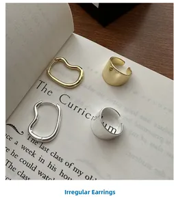 Detailed view of minimalist wavy silver and gold earrings on a vintage book page