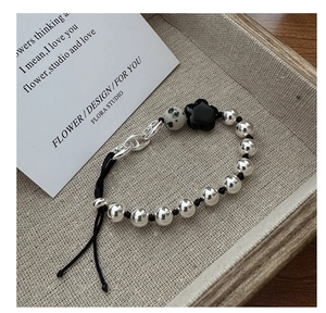 Detail of S925 silver beaded bracelet with flower charm and spotted stone on woven tray