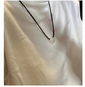 Close-up of minimalist silver heart pendant worn with a simple black cord necklace