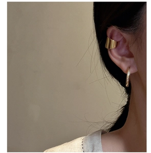 Close-up of stylish gold wave ear cuff and minimalist hoop earring on a female model
