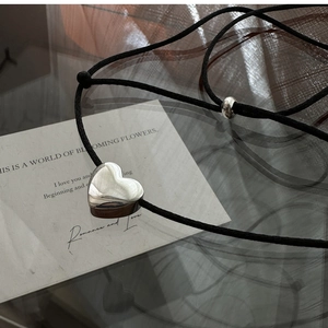 Detail of the polished silver heart pendant on a black adjustable cord over a quote card
