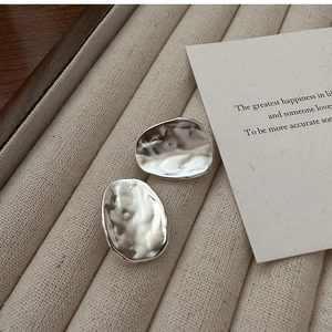 Detail of s925 silver irregular oval earrings with hammered texture on a beige tray