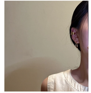 Close-up of golden wavy cuff earring and U-shaped drop earrings worn on ear