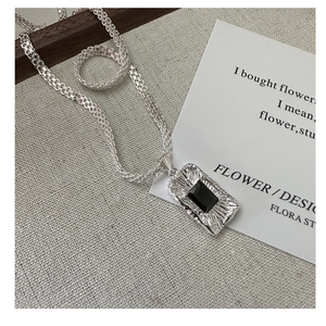 Macro detail of silver necklace with rectangular black zircon on a woven chain