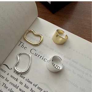 Detailed view of silver and gold wave hoop earrings and thick rings on book pages
