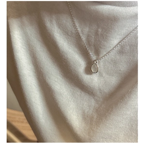 Close-up of a minimalist S925 silver necklace with a round opal pendant on knit fabric