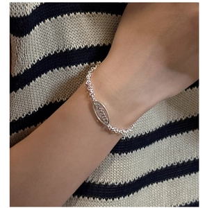 Detail of silver S925 chain bracelet featuring an oval oyster engraved pendant on wrist