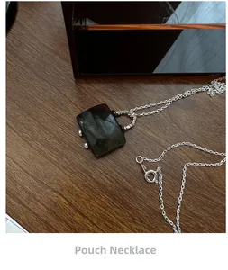 Close-up of a silver handbag pendant necklace with a dark gemstone on a wooden surface