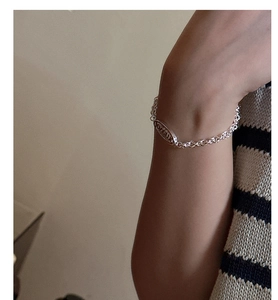 Detail of silver chain bracelet with oval logo tag worn on wrist over knit sweater