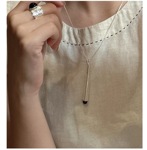 Gros plan sur pendentif minimaliste en argent et bague large avec pierre noire