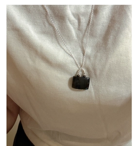 Detail of S925 silver necklace with black handbag shaped pendant on a white shirt