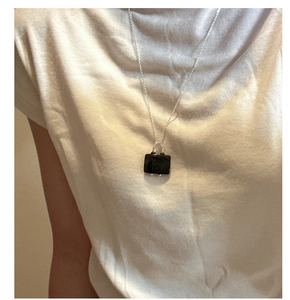 Detail of silver S925 necklace featuring a sleek black rectangular pendant on white t-shirt