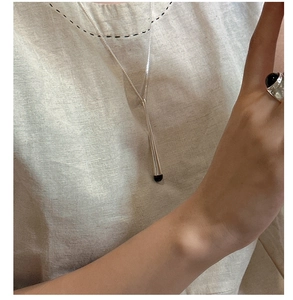 Gros plan d'un collier barre en argent S925 avec émail noir sur vêtement en lin beige