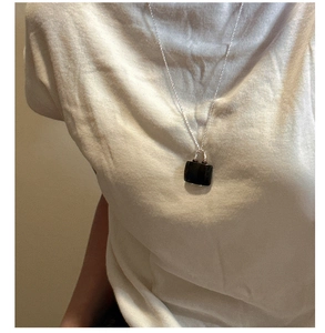 Close-up of S925 silver necklace featuring a sleek dark rectangular pendant on white shirt