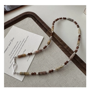 Detailed close-up of S925 silver beaded necklace with earth-toned stones on linen board