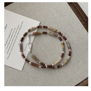 Macro detail of S925 silver necklace with brown agate beads and metallic accents